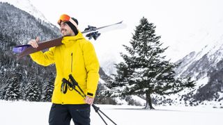 A skier in a yellow jacket holds his skis over his shoulder