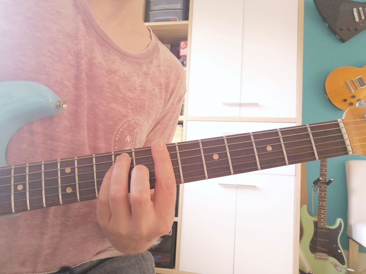 A person playing the E-shape B major barre chord on guitar