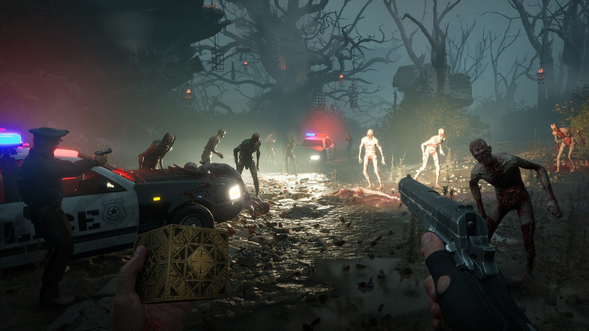 The player holds the Genesis Configuration in their left hand and a pistol in their right as they aim at approaching zombie-like enemies in Clive Barker's Hellraiser: Revival, a backup police officer nearby alongside other police cars - the surrounding forest is dark and filled with hanging cages from tree branches.
