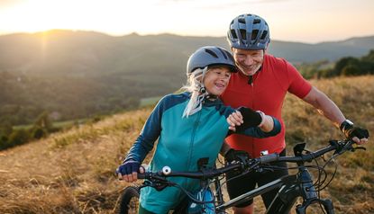 Portrait of beautiful senior couple on bike ride in autumn nature. Checking performance and route on smartwatch.