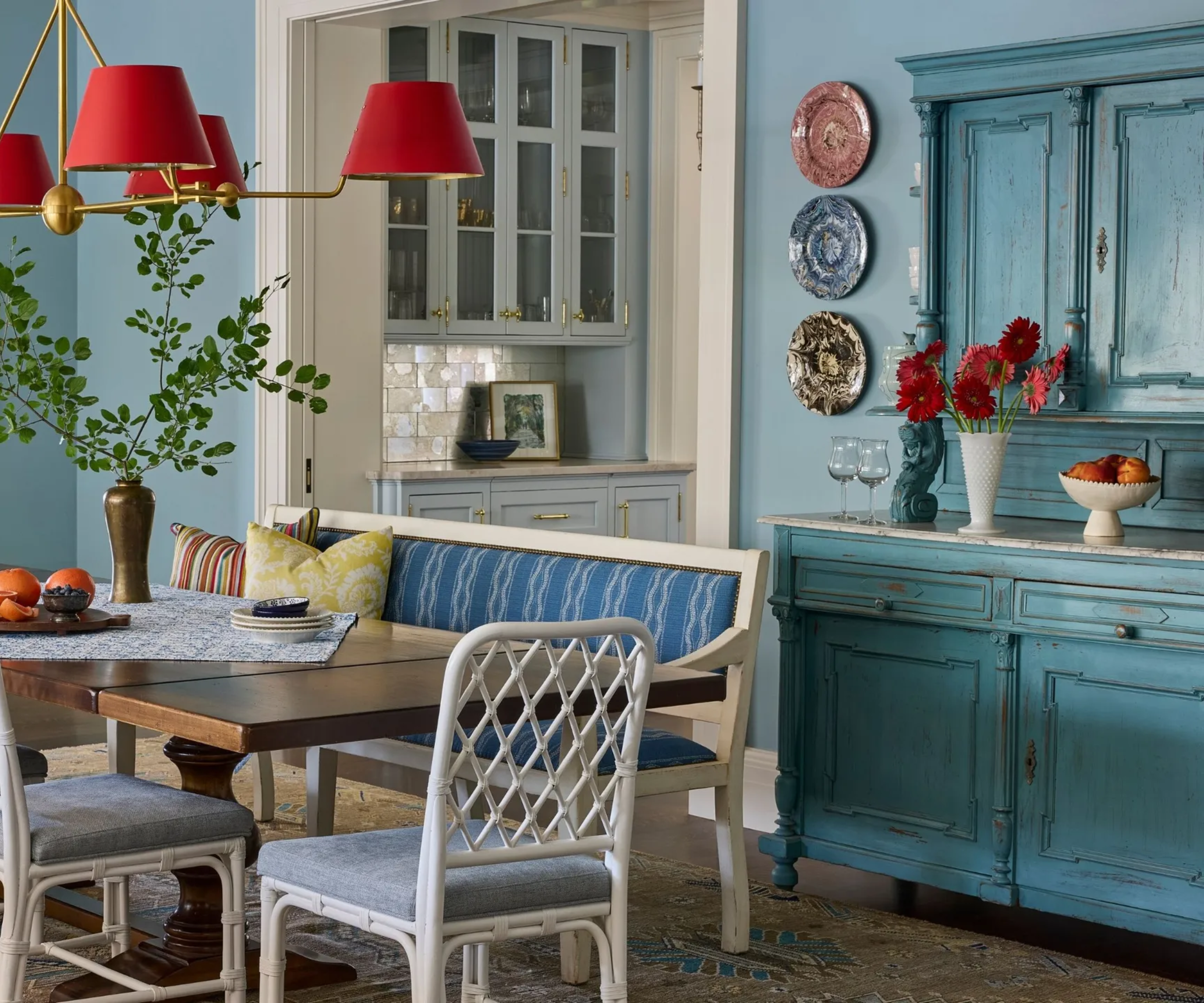 a dining room painted blue with a rustic blue cabinet to the right and a dining table with a bench and chairs in the middle