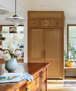 A large wood-paneled fridge in a kitchen, with a vase of flowers on the countertop.