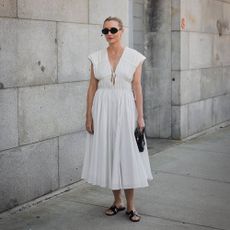 Kristen wears white summer dress black clutch and black slides. 