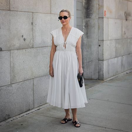 Kristen wears white summer dress black clutch and black slides. 