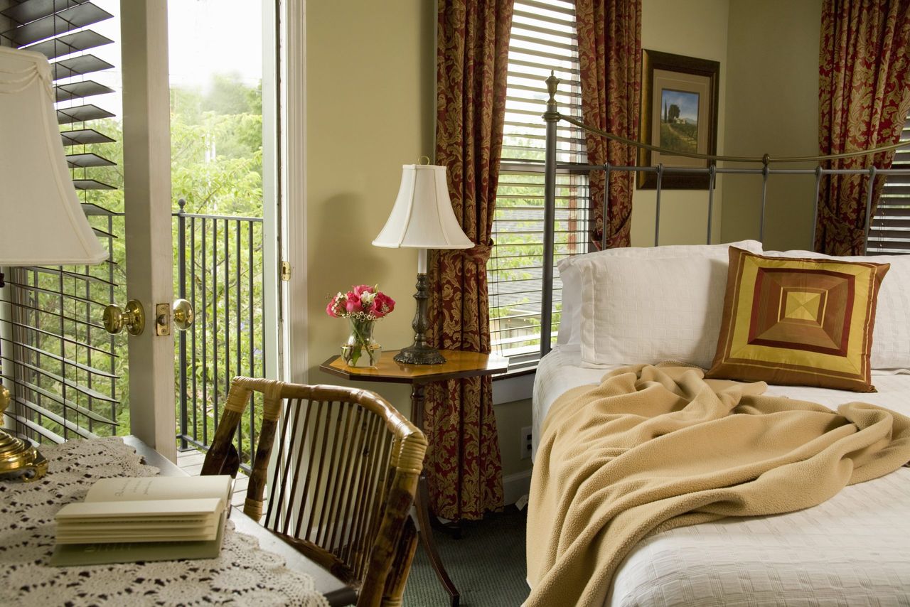 Bedroom with desk next to iron cast bed with open doorway and Venetian blinds. (Photo by: Jumping Rocks/Universal Images Group via Getty Images)