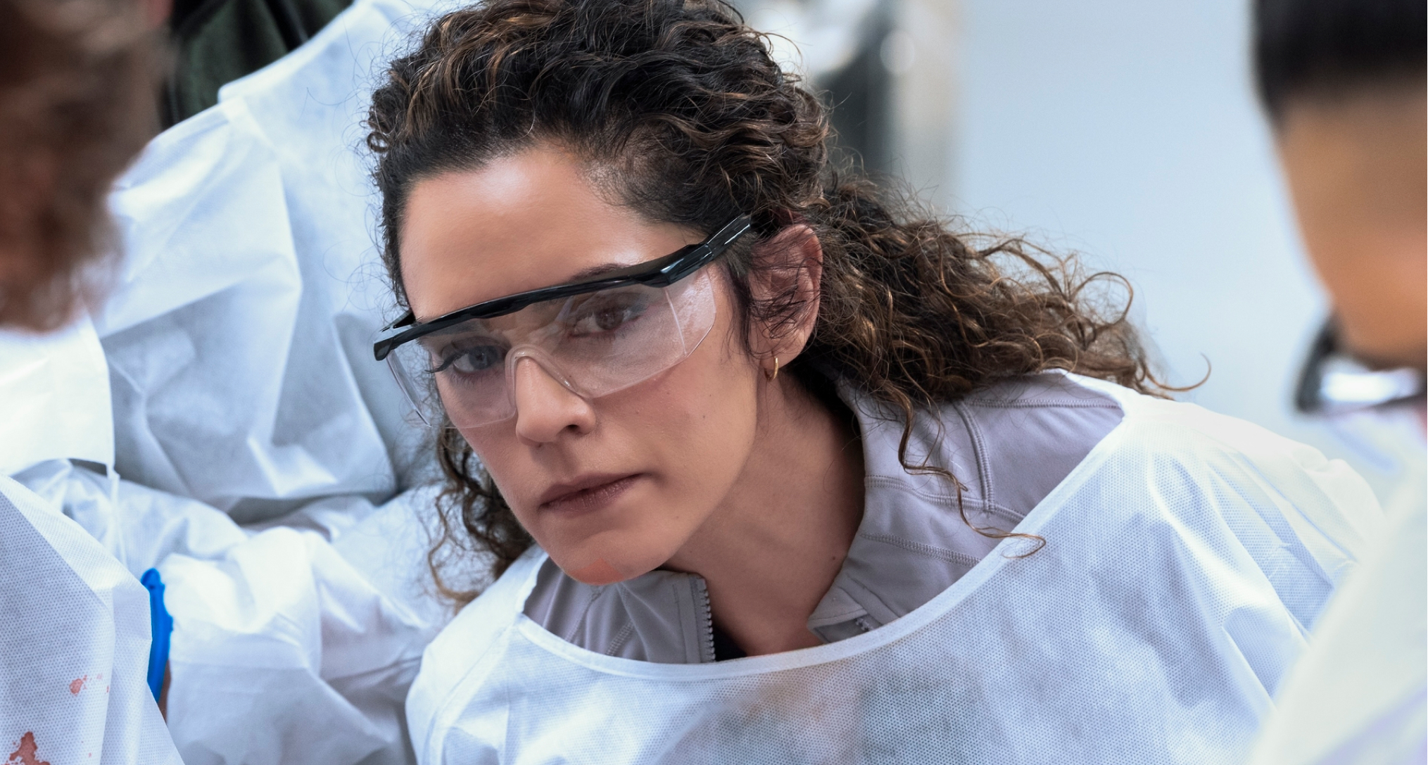 Sepideh Moafi as dr. al-hashimi wearing goggles and a white cover up while in surgery in a still from the pitt season 2