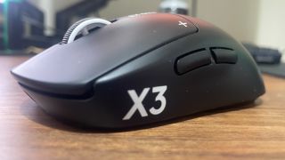 A Logitech G Pro X3 Superstrike gaming mouse on a wooden desk.