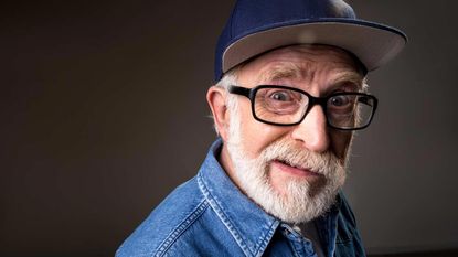 A man with a white beard and a ball cap looks dismayed.