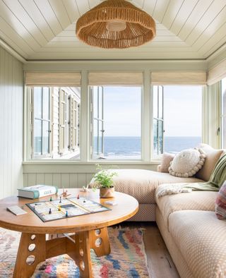 snug with green panelling, neutral chaise, colorful rug and wooden table