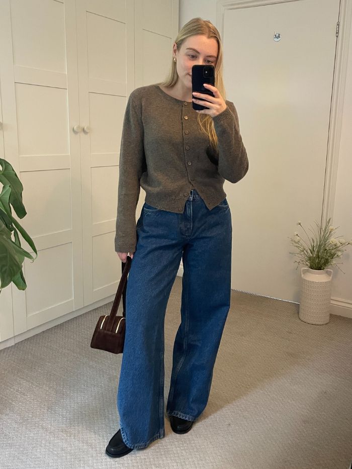 Woman wears brown cardigan, blue jeans and black loafers