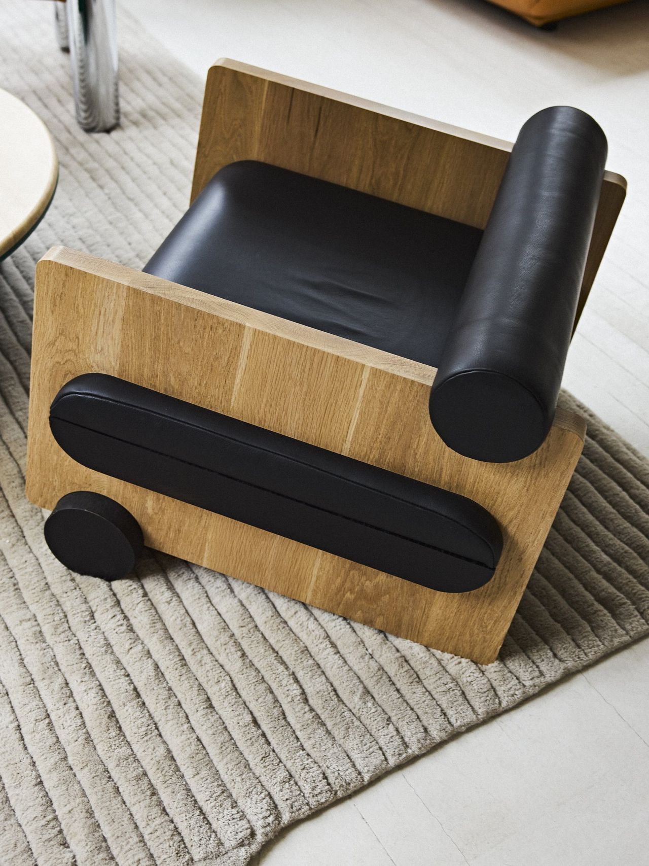 A mid-century modern-inspired wood and leather chair in brown and black sits on top of a fluffy grey rug in a naturally lit room.