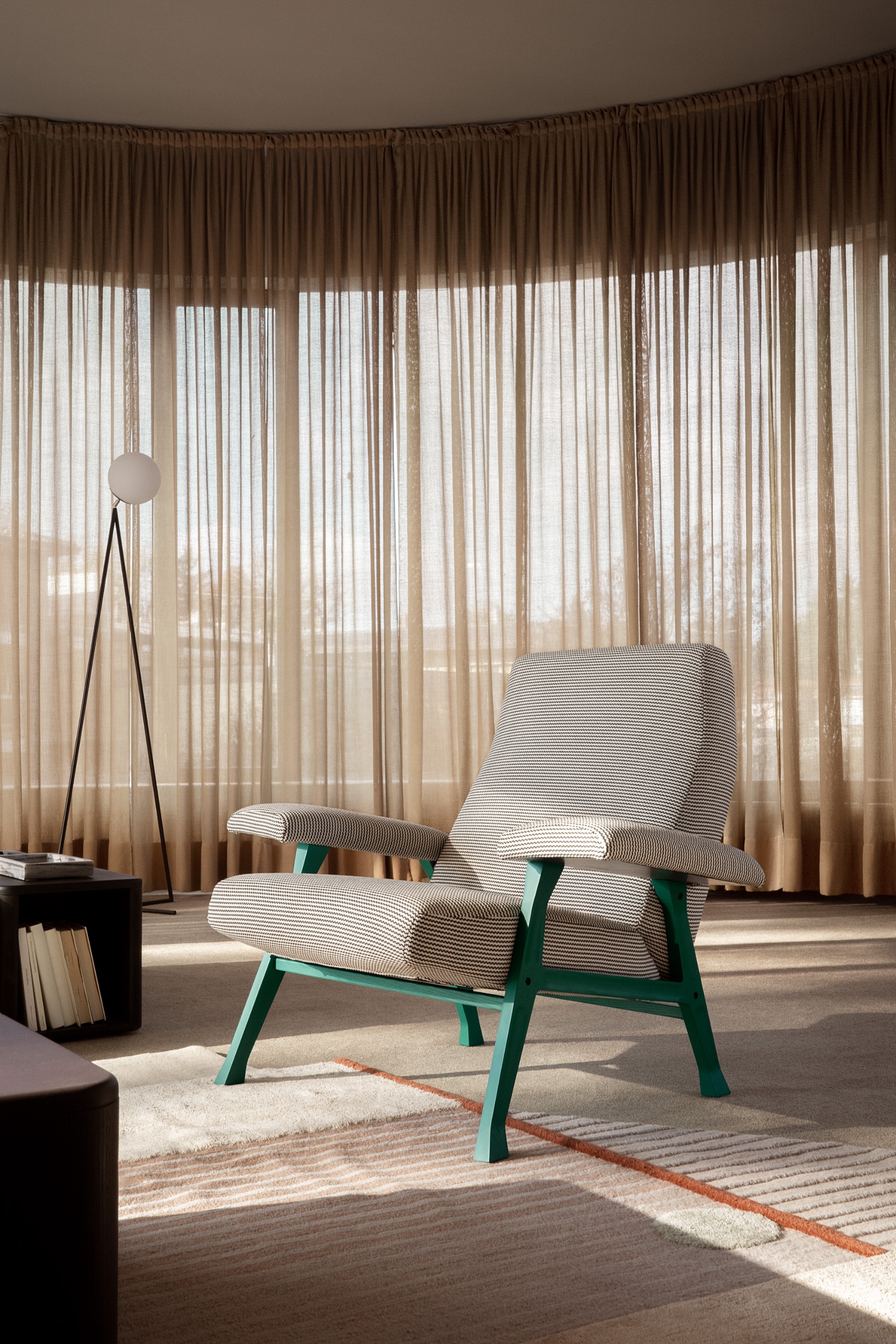 An armchair with a green base sits on top of a rug in a room with pulled beige sheer curtains right the way around it