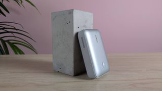 Aukey Spark Mini 20000 leaning on plinth on desk with pink wall and plant in background