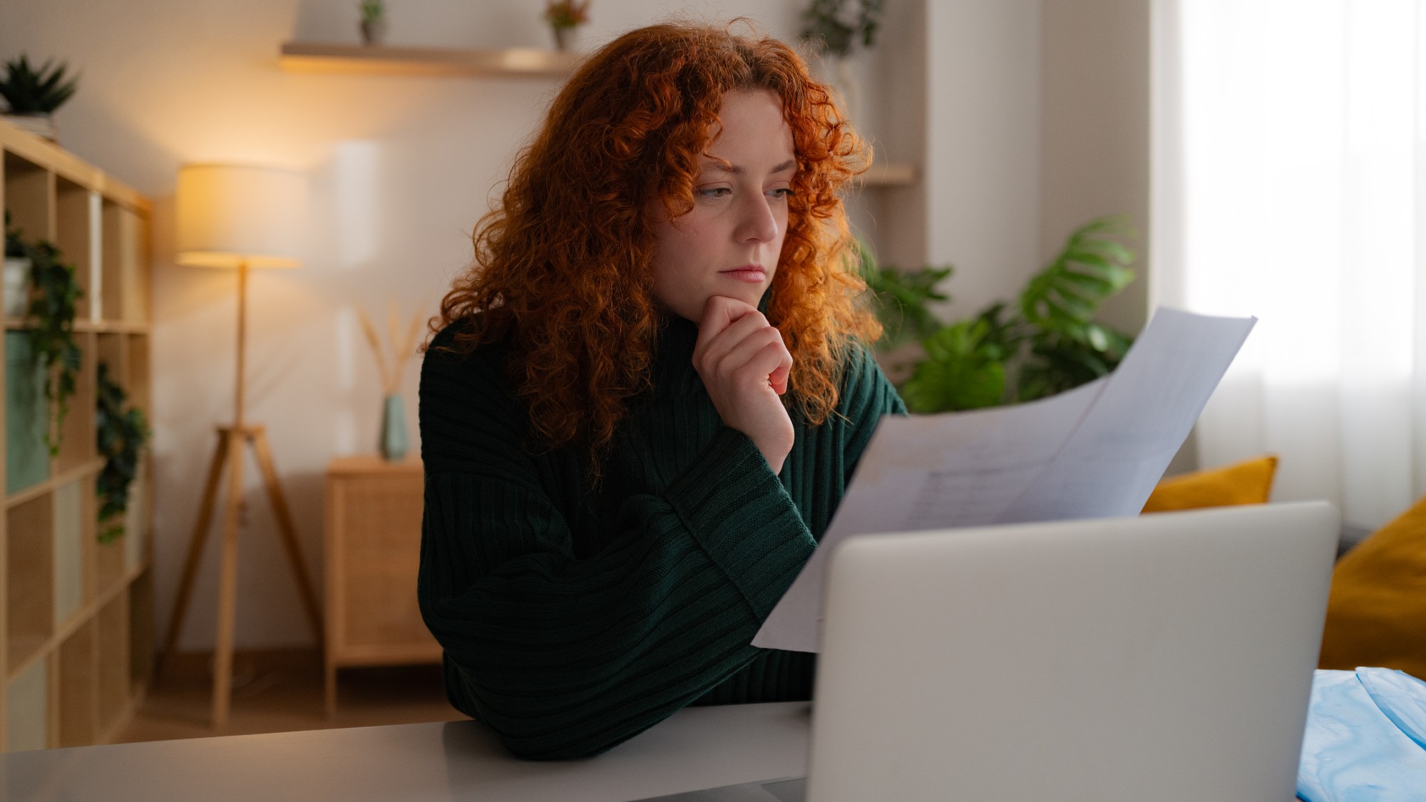Young woman sitting at a desk in front of her laptop and studying papers