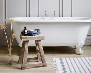 small wooden stool in a bathroom with free-standing white tub and white wall and floorboards