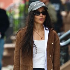 Zoe wears a baseball cap, white tank top and a suede jacket.