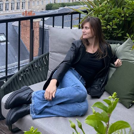 French editor and writer Eugenie Trochu poses on a terrace in Paris wearing a black leather blazer, black top, straight-leg jeans, and black lug-sole boots