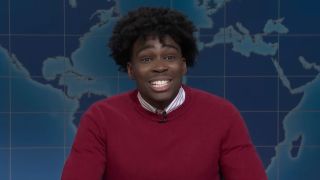 Kam Patterson dressed in a red sweater talks to SNL on Weekend Update.