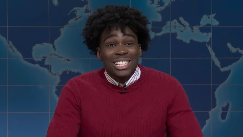 Kam Patterson dressed in a red sweater talks to SNL on Weekend Update.