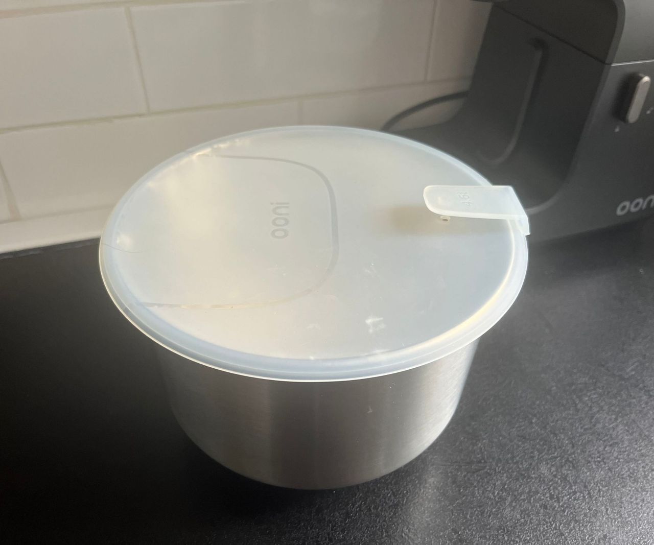 A metal bowl on a black kitchen counter with a white silicone lid on top
