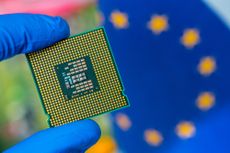 A gloved hand holds a semiconductor chip with an EU flag in the background