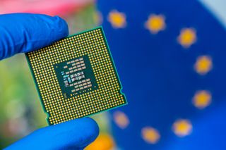 A gloved hand holds a semiconductor chip with an EU flag in the background