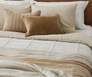 Magnolia bedding in neutrals, layered with cushions and blankets