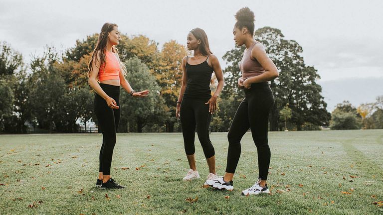 A group of three women are pictured in a luscious green park in their best workout and exercise gear with crop tops and leggings