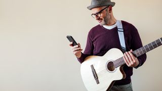 Man holding a phone while standing with an acoustic guitar