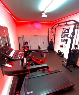 A garage converted into a home gym with red strip ceiling lighting and lockers