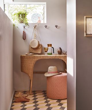 A simple bathroom with light purple walls, a rattan dressing table and mosaic floor tiles