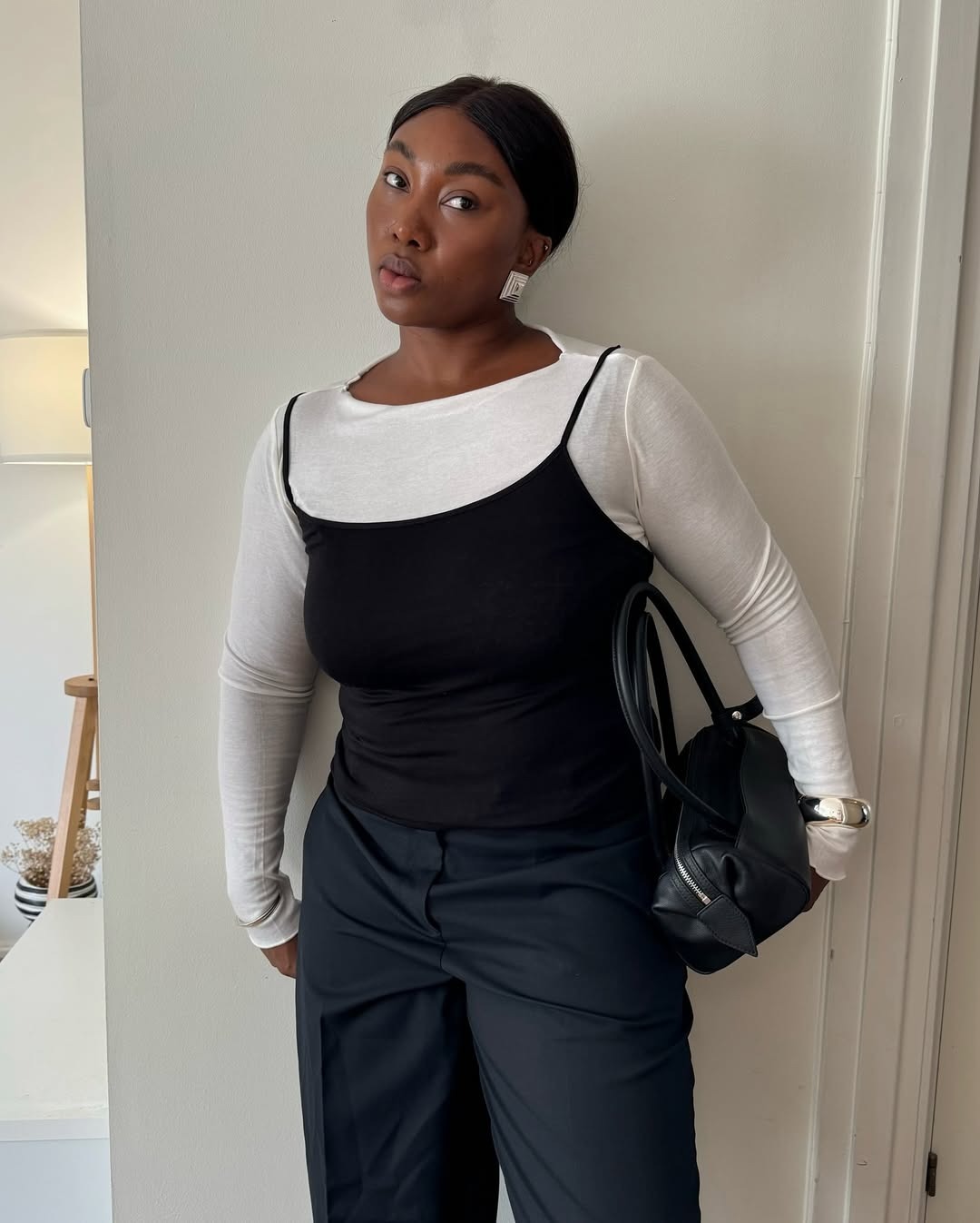 Influencer Nnenna wears a white long sleeve under a black tank and a black trousers.