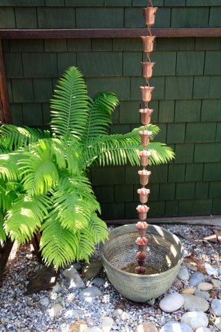 An ornamental rain chain falling into a bucket where rain water is collected