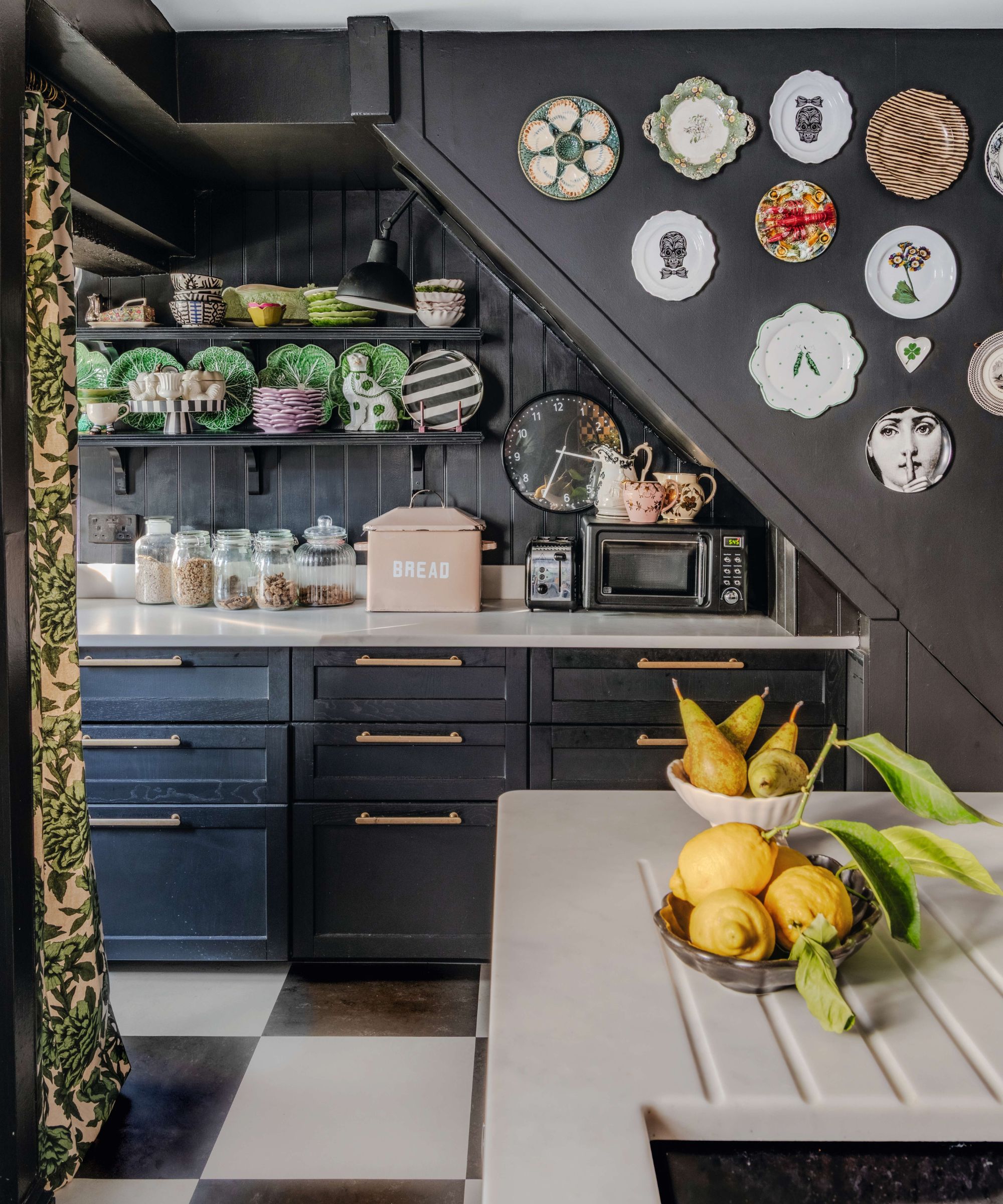 a small dark black painted kitchen beneath sloped ceilings with open shelvings with vintage crockery and a plate wall