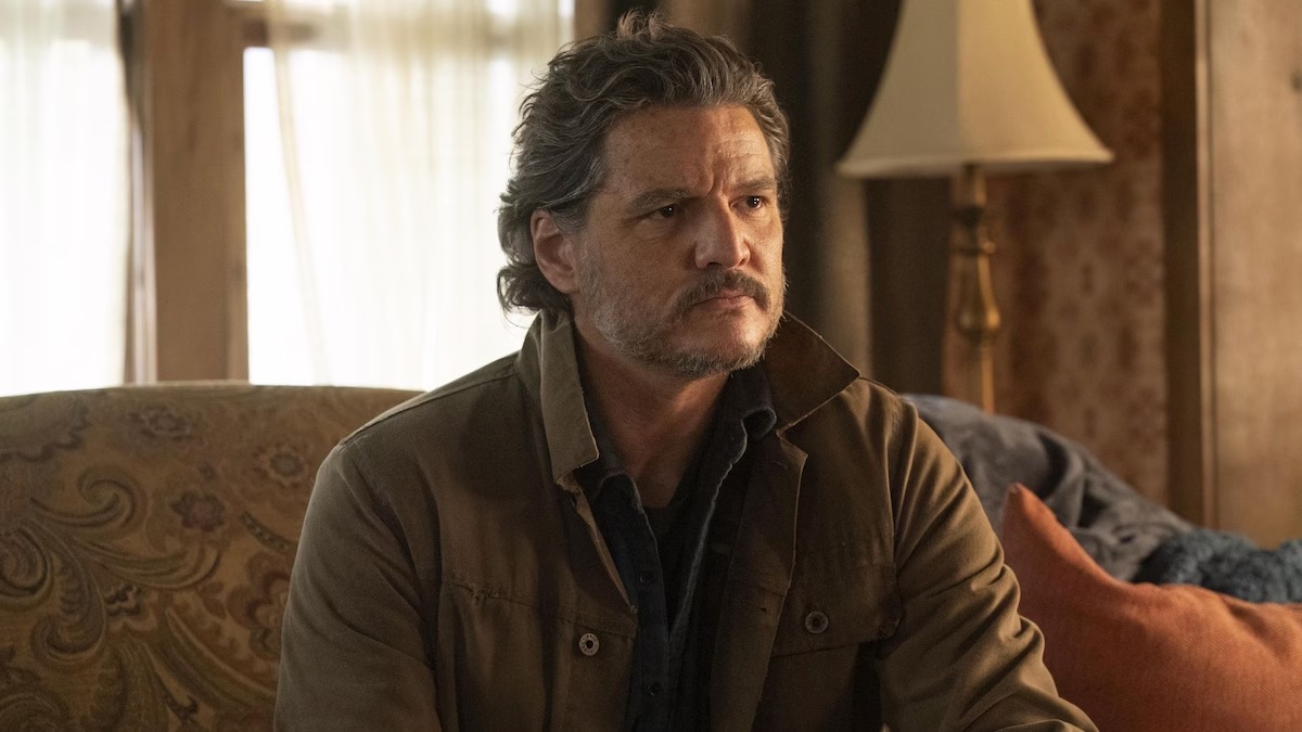 A bearded man in a brown jacket sitting on a sofa in a lounge.