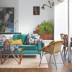 A living room with a beige, natural texture rug, a velvet emerald green sofa and a round glass coffee table