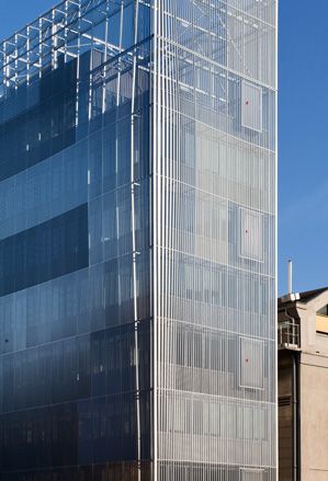 A closer look at the corner of the Voltaire building photographed while still under construction. Multiple stores, rectangle-shaped building, with panoramic windows on each floor.