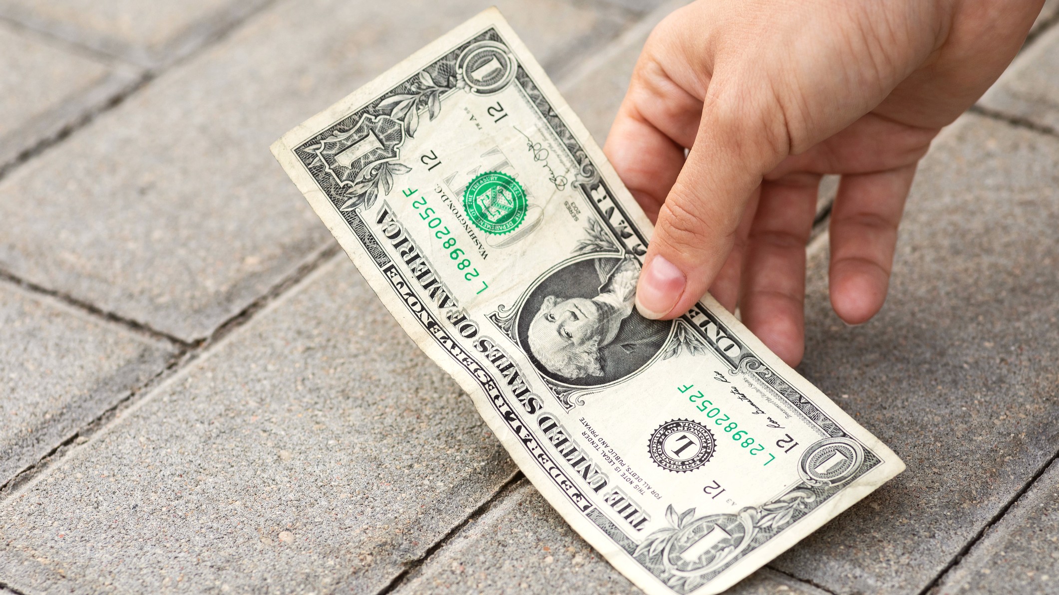 Lost and found money. A man is picking up a one-dollar bill from the ground, representing $1 more.