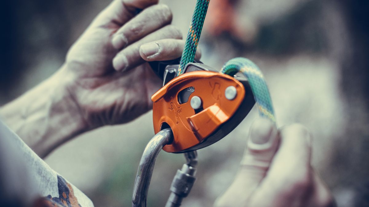 A man&#039;s hands operating a belay device