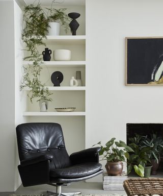 corner of living room with white walls with shelving, black leather swivel chair, lots of plants