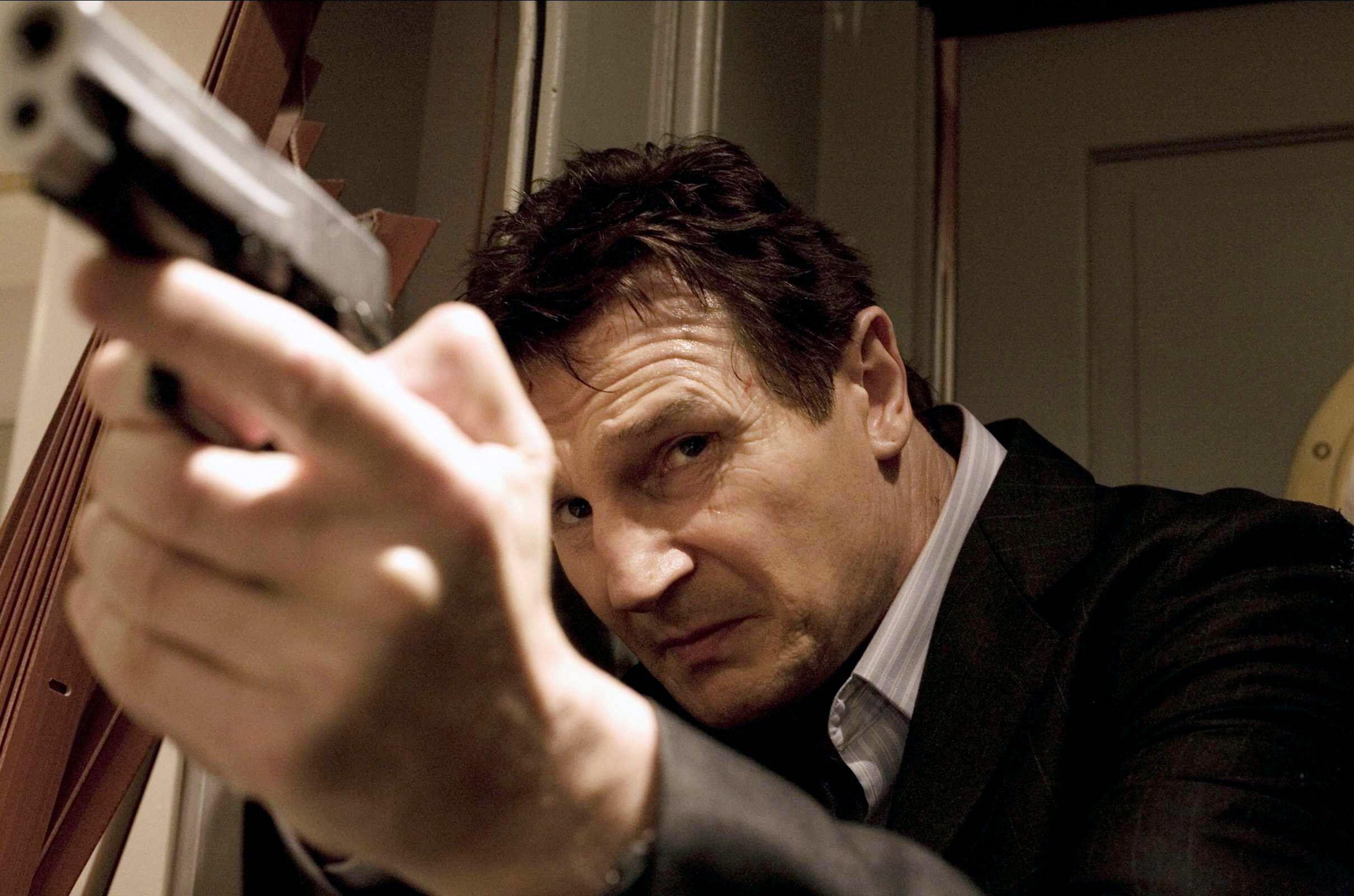 Liam Neeson aims a gun upward in Taken