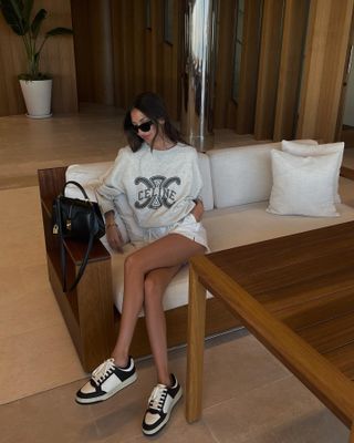 Woman wears a Celine logo sweatshirt, white drawstring shorts and black and white sneakers.