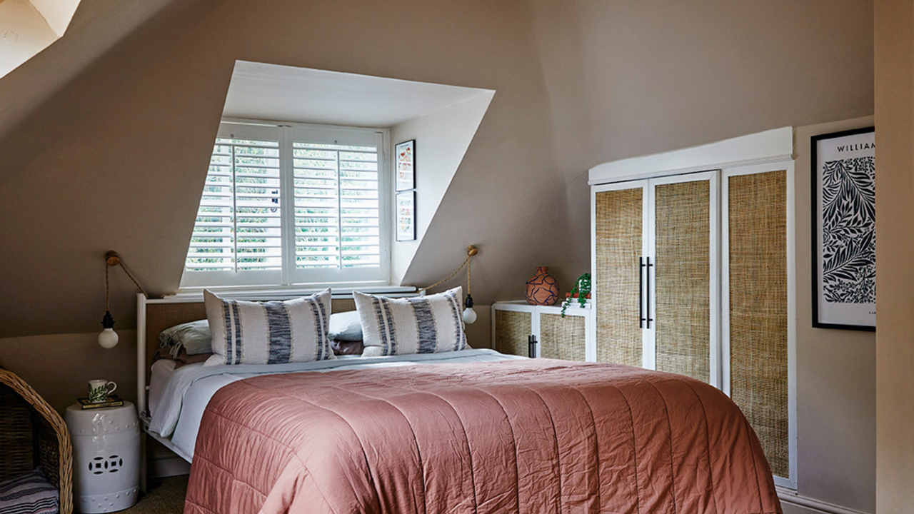 Warm toned bedroom, with bed under a dormer window and sloped ceilings