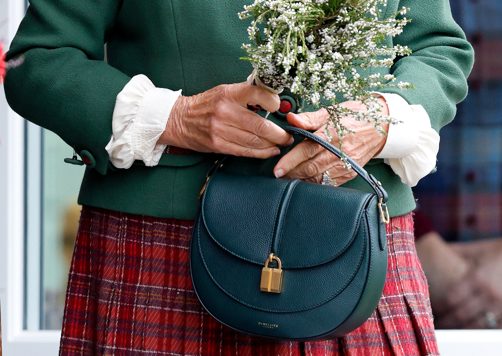A closeup of Queen Camilla's hands holding a green saddle bag and flowers