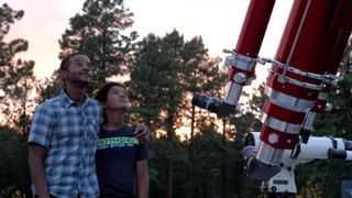 Two people in front of a telescope, looking up at the sky.