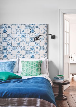 Bedroom with blue patterned headboard and wall light and view to freestanding bath in en suite bathroom