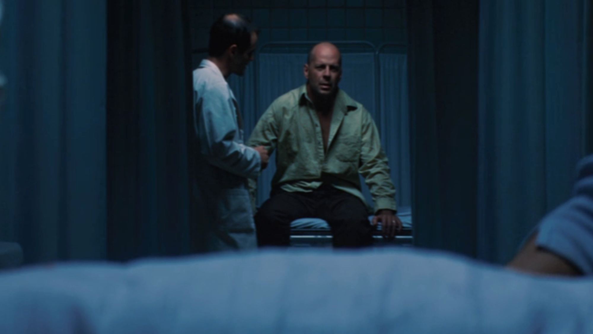 Bruce Willis sitting on a hospital bed in the background behind a doorframe in Unbreakable