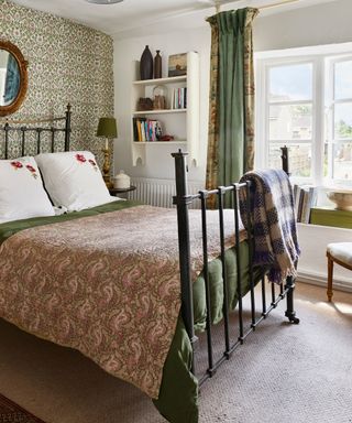 country style bedroom with wrought iron bed frame, patterned wallpaper and bedspread and window seat