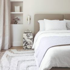 A light-coloured bedroom with built-in shelves and a fabric headboard on the bed