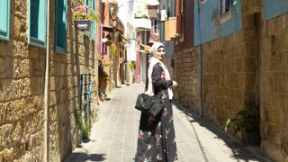 Generate speaker Sara Soueidan walks down a quiet street in Lebanon, looking back at the camera over one shoulder.